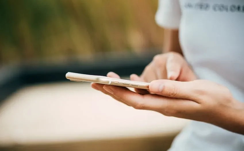 Seorang wanita tersenyum sambil menggunakan smartphone-nya di rumah.